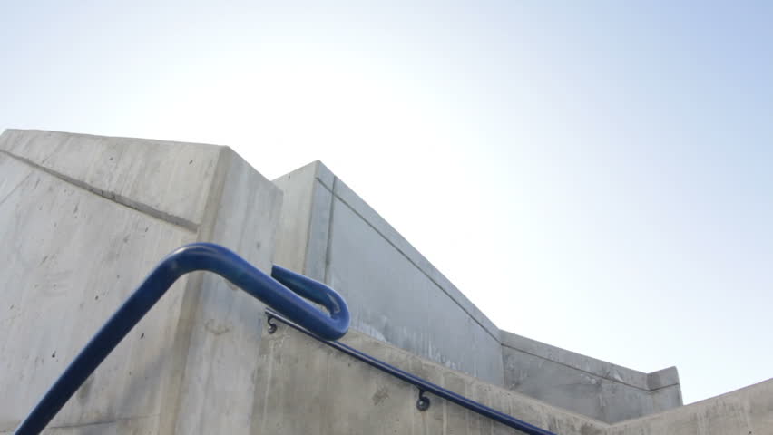 A free runner man jumps off stairs towards camera then jumps over a wall and down to the ground