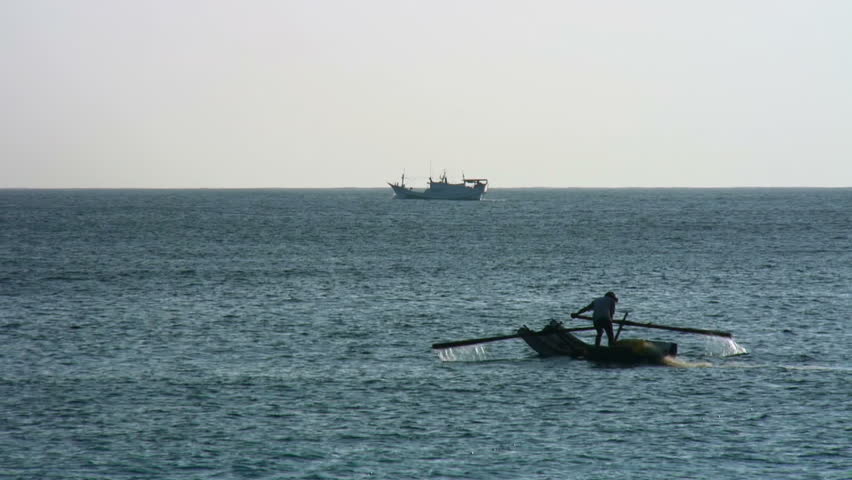Man doles out net in while a fishing boat cruises by 