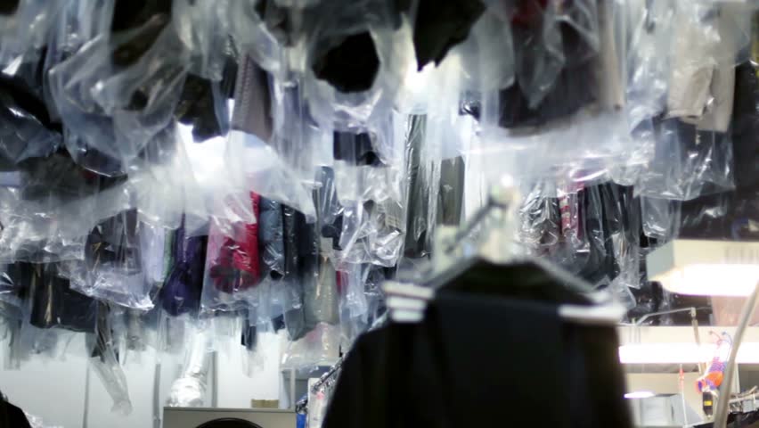 Many clothes in polyethylene slipcovers hang and move in dry cleaning
