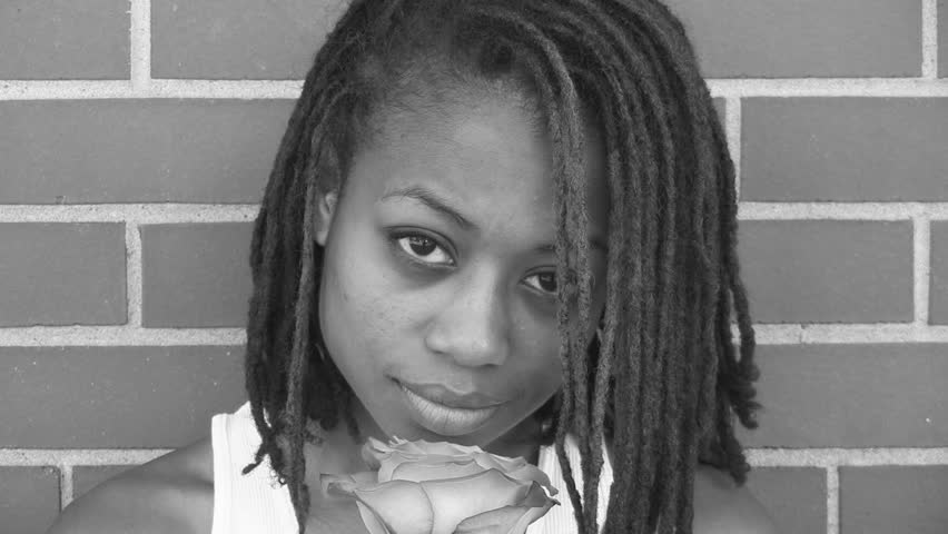 A sad and pretty girl smiles as she smells a rose. Black and white.