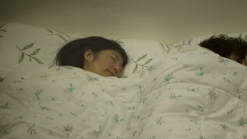 Low key timelapse of a couple in bed; the man is sleeping, but the woman is suffering from insomnia and tosses and turns.
