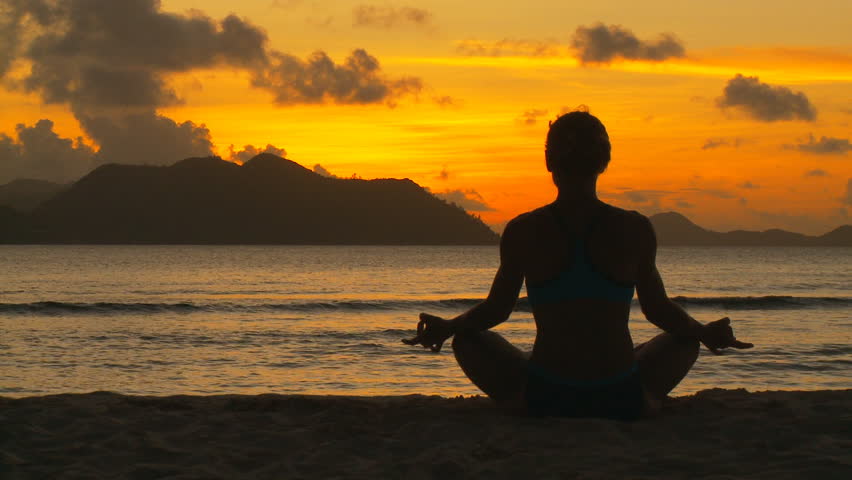 young woman in lotus seat on beach at tropical sunset