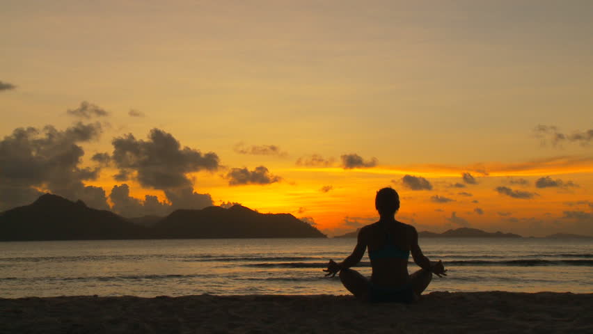 woman on beach in meditation at tropical sunset