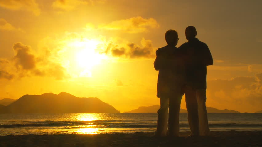 elderly couple cheering on beach at sunset
