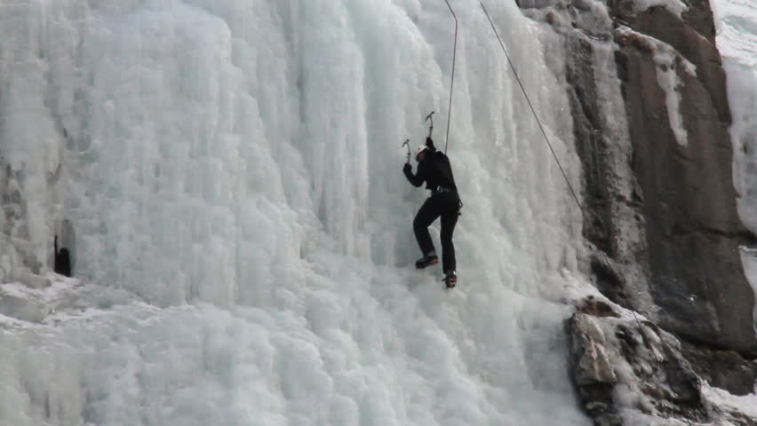 Mountain climber ice climbers on steep frozen waterfall high in Wasatch Mountains, Utah.