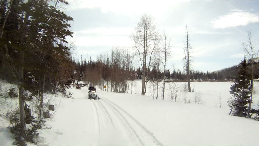 Snowmobile sled follow rider through high mountain forest during winter snow. Aspen and pine trees and beautiful blue sky of central Utah Wasatch mountains. Rocky Mountains.