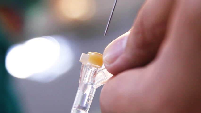 Injecting medicine to IV tube. Out of focus surgeons at the background. Close up.