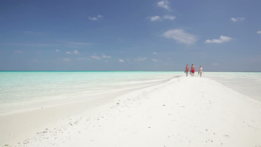 tourists with snorkeling equipment walking on sandbar
