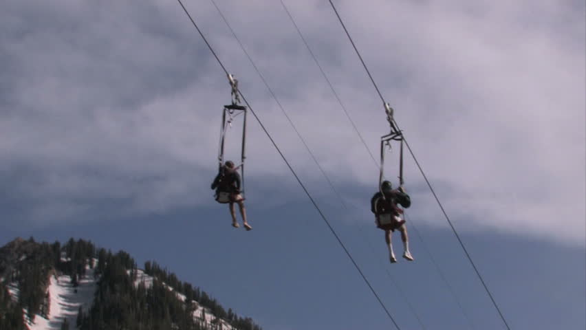 Man and girl quickly sliding down a steep zipline at a mountain resort in Utah. Steep mountain forests with early summer snow melting. Fun, excitement and recreation.