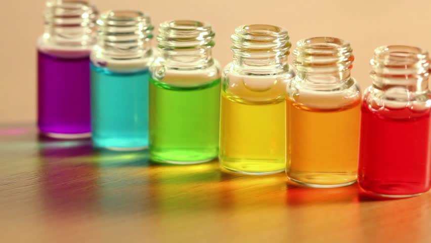 Six transparent open bottles stand in row on wooden surface and moves with color oil on them