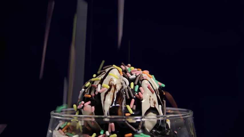 Fudge Sundae (HD). Sundae with fudge poured and color candy sprinkles. Finished with a cherry faded in from the same shot.