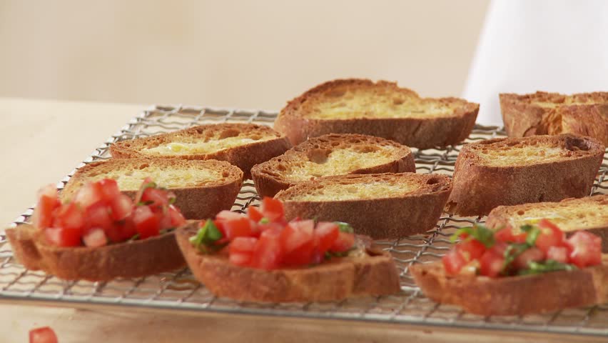 Baguette slices being topped with a tomato and basil mixture