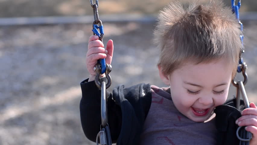 Young toddler boy swinging on a swing at a playground.  Very happy.