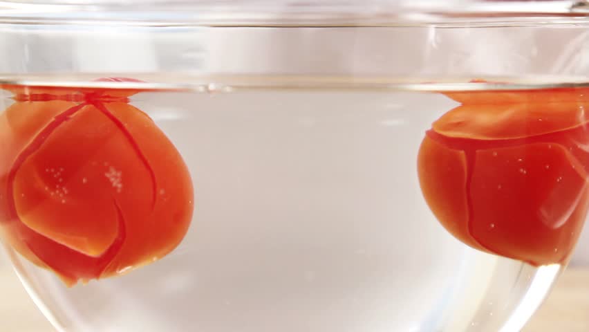 Tomatoes being removed from a bowl of hot water and placed into a bowl of cold water