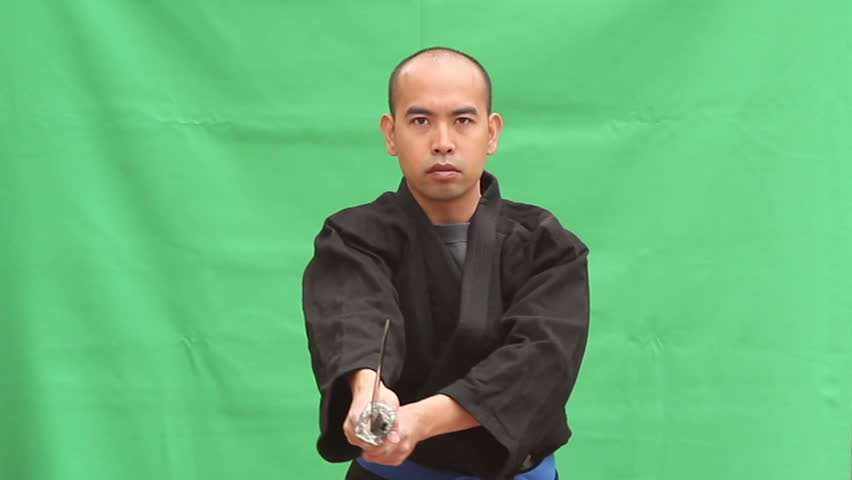 An Asian man in a Japanese Gi draws a Samurai Sword (Katana), and slashes through the air, presents 3 en guarde positions.