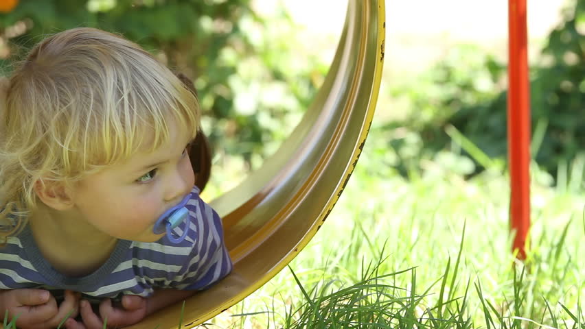 Cute and carefree toddler swinging in barrel swing (jungle gym) - thoughtfully looks around at this new experience!