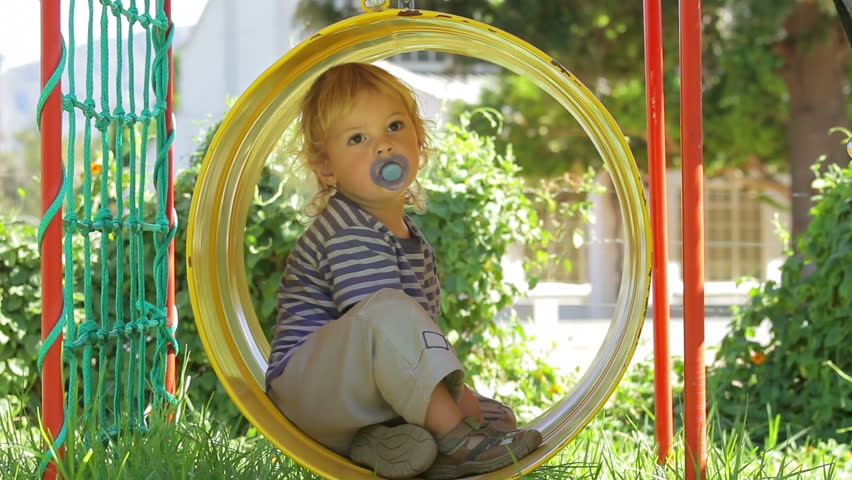 Carefree toddler swinging in barrel swing (jungle gym) - thoughtfully enjoying this new experience!