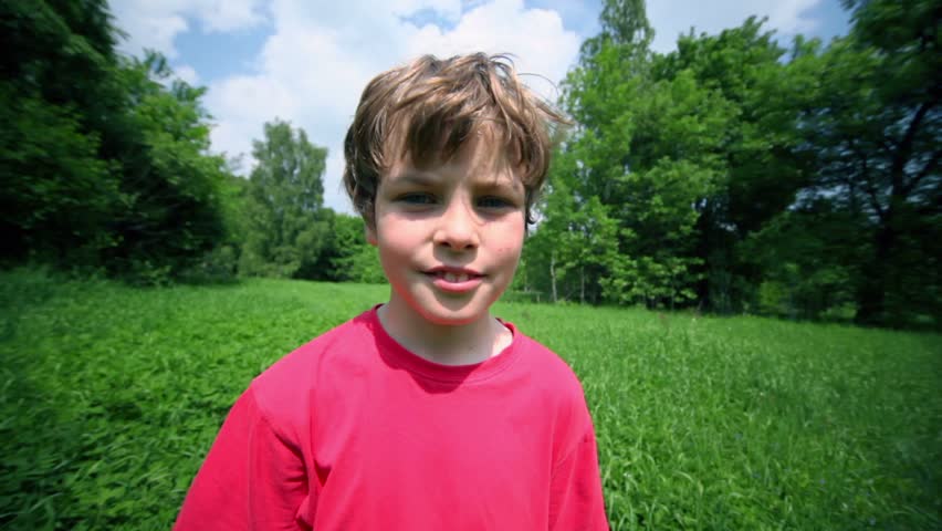 Little boy walks by grass glade under blue sky with clouds, closeup view