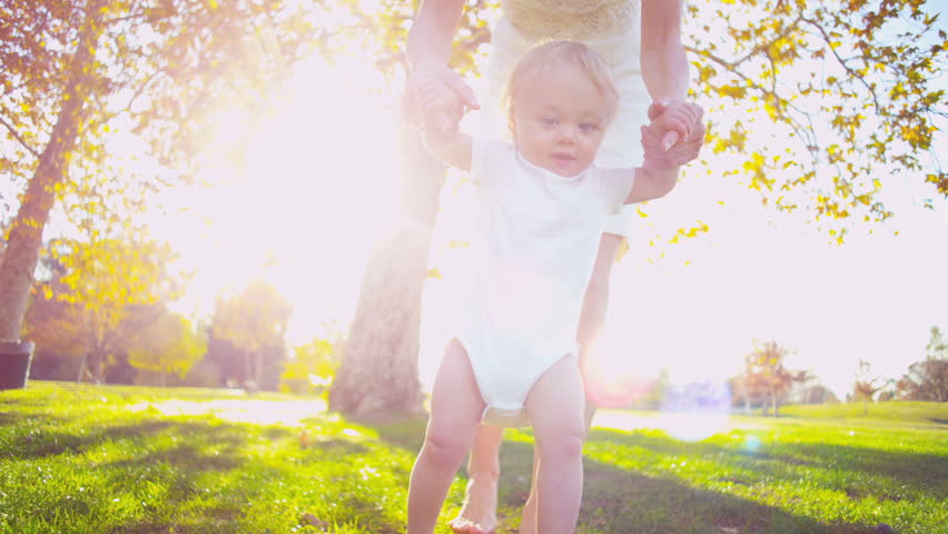 Cute baby being supported by the mother while the baby takes the first steps outdoors