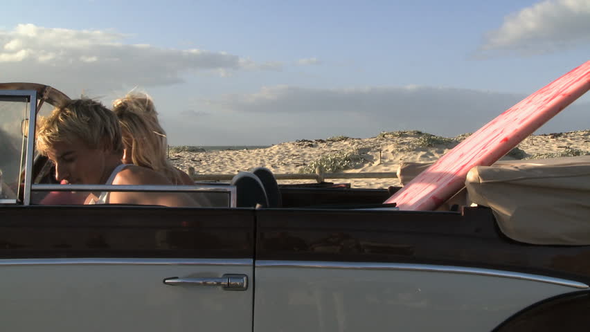 MEDIUM SHOT OF A YOUNG COUPLE GETTING OUT OF A CAR AND PICKING UP A SURFBOARD