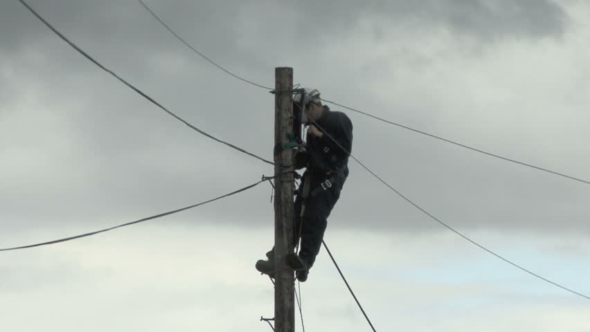 Telephone engineer works at top of pole in rain 1. HD.
