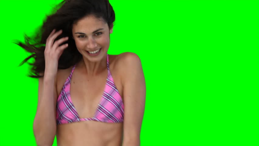 A smiling woman jumping up and down in a bikini while in front of a green background