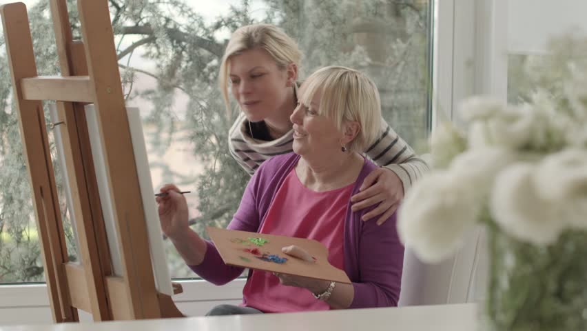 Family portrait of women, with happy mother painting for hobby and daughter smiling and hugging her at home. Dolly shot