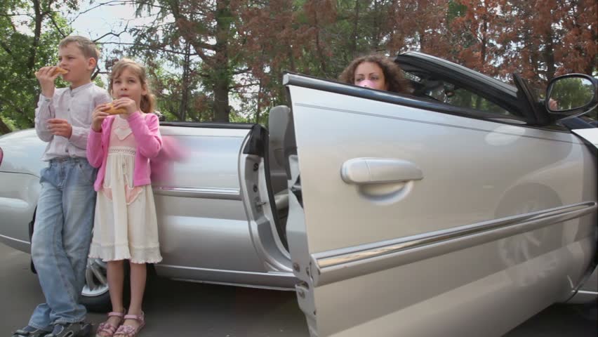Two kids eats bread and drink water near cabriolet, their parents sit with glasses in cabriolet, around motion
