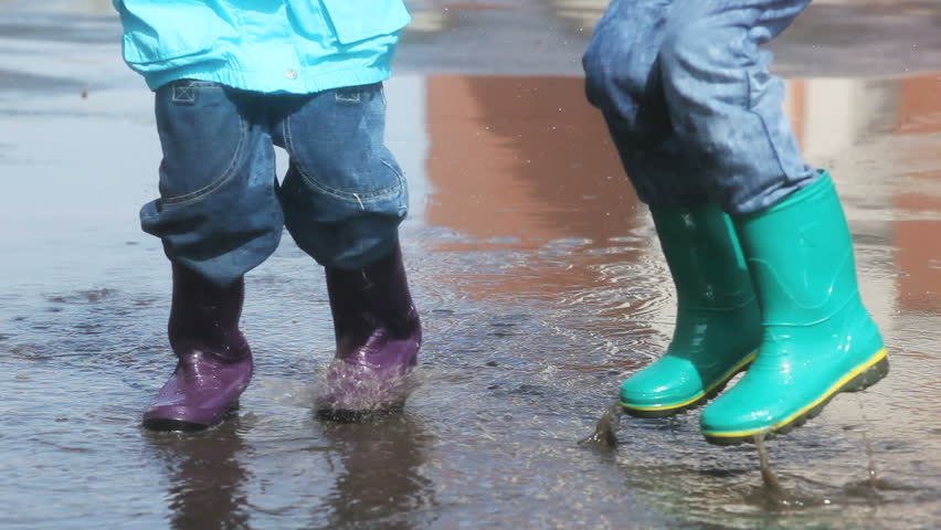 Kids in rain boots jumping chaotically in puddle