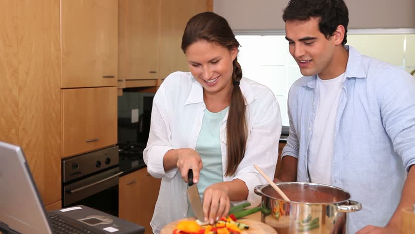 Couple cooking while reading the recipe on a laptop in a kitchen