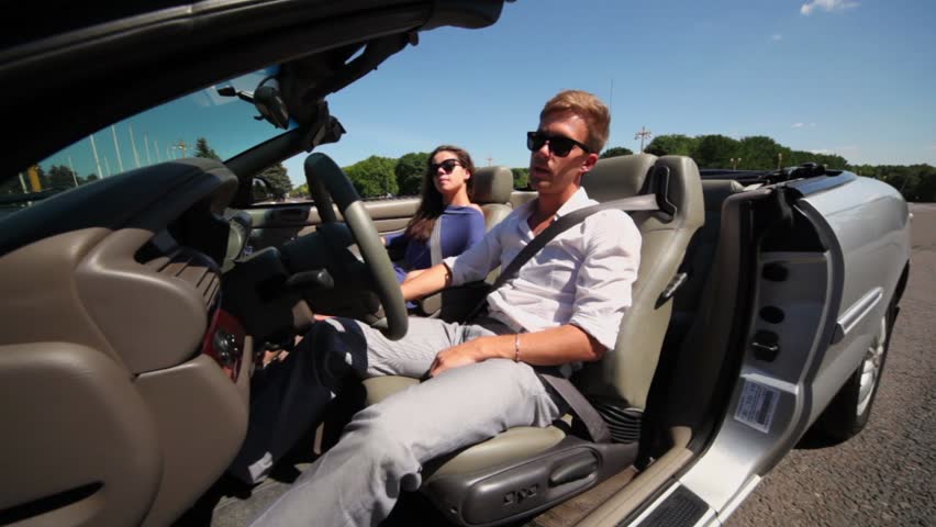 Young couple in sunglasses sit in cabriolet with driver door open at sunny summer day