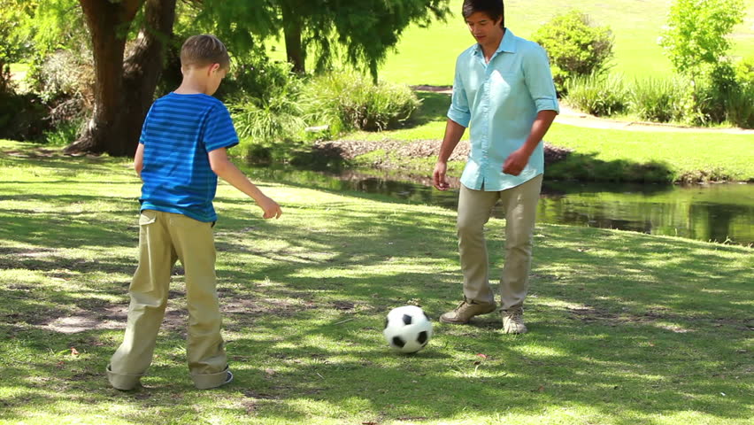 Smiling man playing soccer with his son in a parkland
