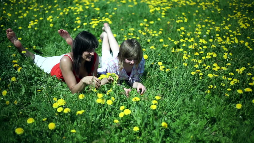 Mother and daughter lying on meadow and making a garland