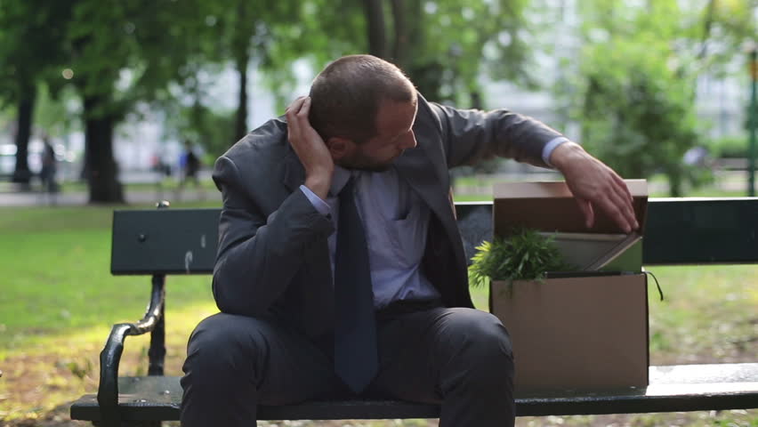 Just fired, unemployed sad young businessman sitting in the city park

