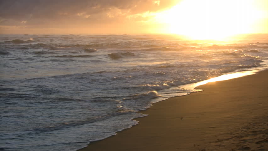 Waves gently wash up onto the beach, then recede as the sun starts to rise. (High Definition)