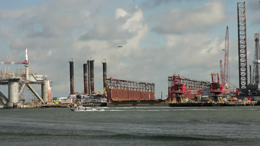 Two boats speed by oil and gas industrial drilling platforms, and rigs in for repairs and other servicing.