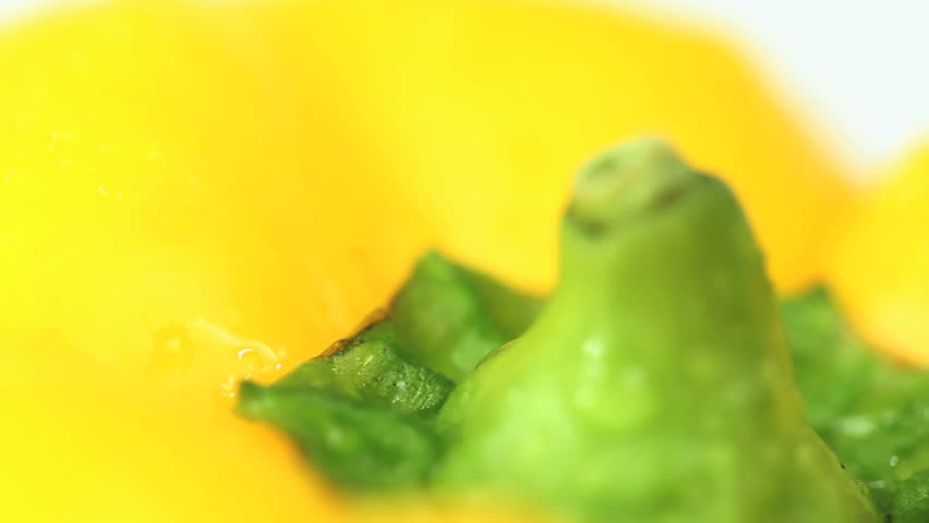 Closeup of a big yellow paprika top rotating slowly on white background, yellow bell pepper is sprinkled with water drops that sparkle nicely as they come into focus.