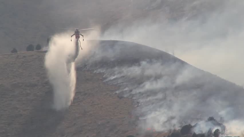 A helicopter battles a gigantic wildfire on a dry mountainside, dropping hundreds of gallons of water on the flames.