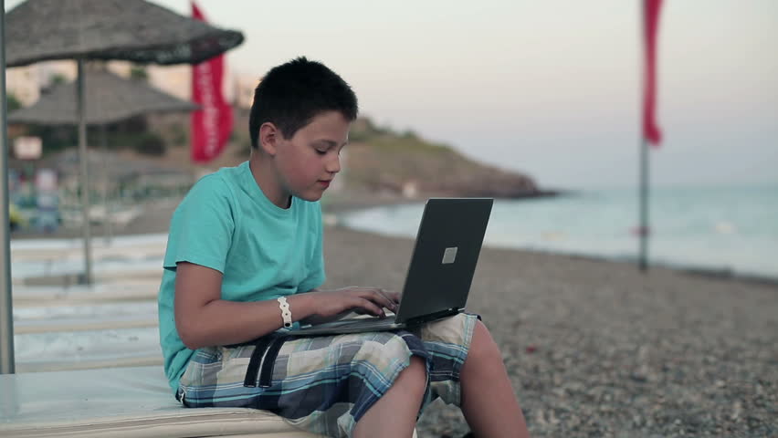 Young happy teenager with modern laptop on the beach
