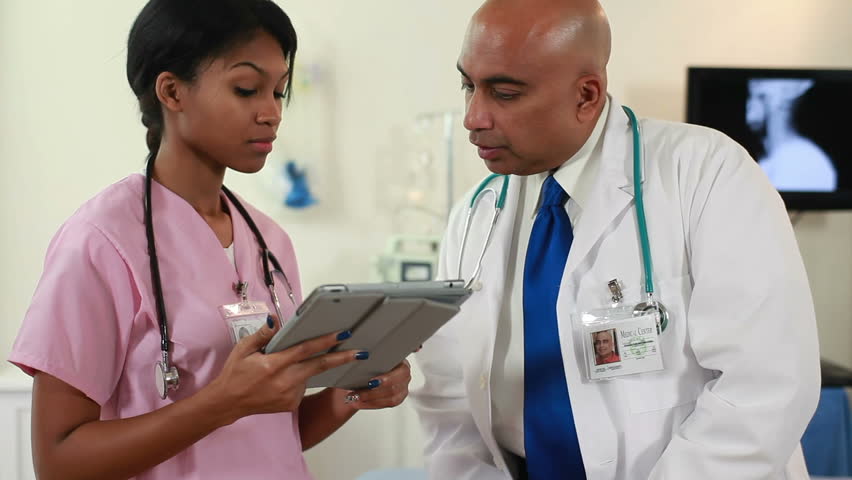 Indian physician with pretty African American nurse using electronic tablet stop discussion and smile for camera.