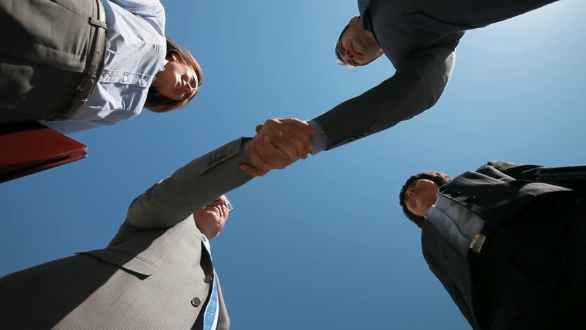 Smiling business teams performing a cross handshake