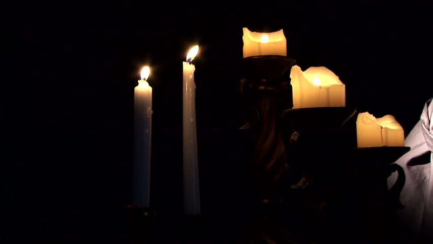 A dolly shot across lit candles ending with a cloaked and masked 