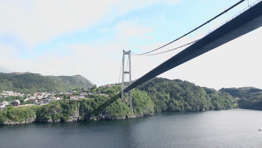 Huge pendant bridge at coast with houses among forest on mountains under cloudy sky