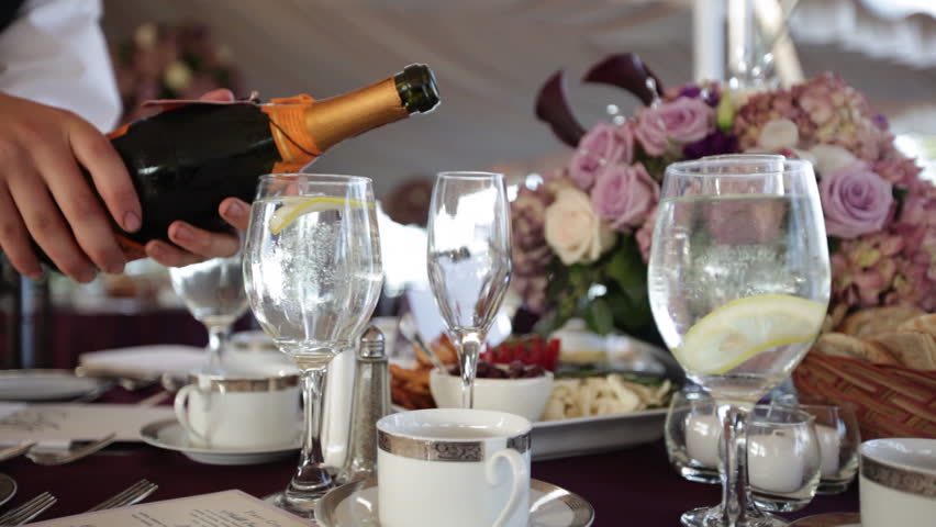 a waiter pours champagne at a wedding reception under a tent