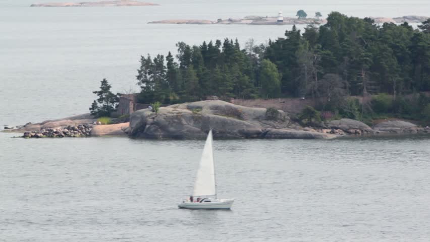 Yacht sail beside rocky coast with beacon and forest at summer day near Helsinki
