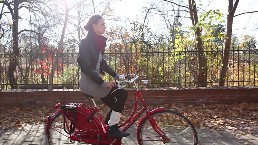 Young woman riding on bike in autumn setting.
