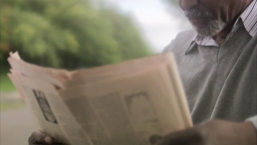 A man sitting on a bench reading a newspaper