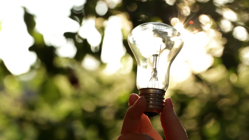Sun rays are going through the light bulb in a girl's hand. Shallow dof