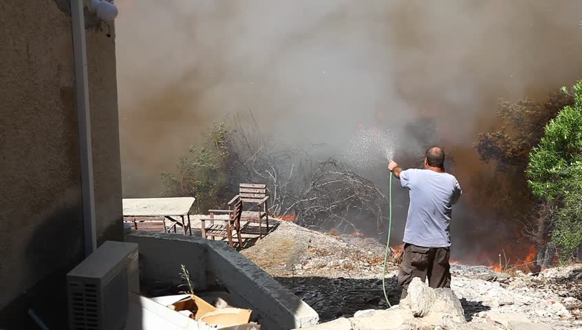 TIVON, ISRAEL - AUGUST 09: A man tries to save his home from burning after a forest fire breaks out in Kiryat Tivon. Rescue workers struggle to prevent further damage. Tivon, Israel August 09, 2012