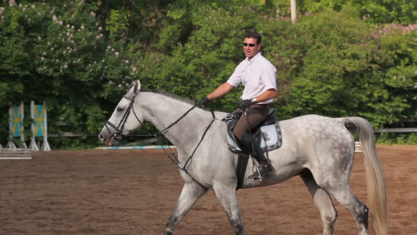 Horseman rides on horseback by equestrian field and says something at sunny summer day